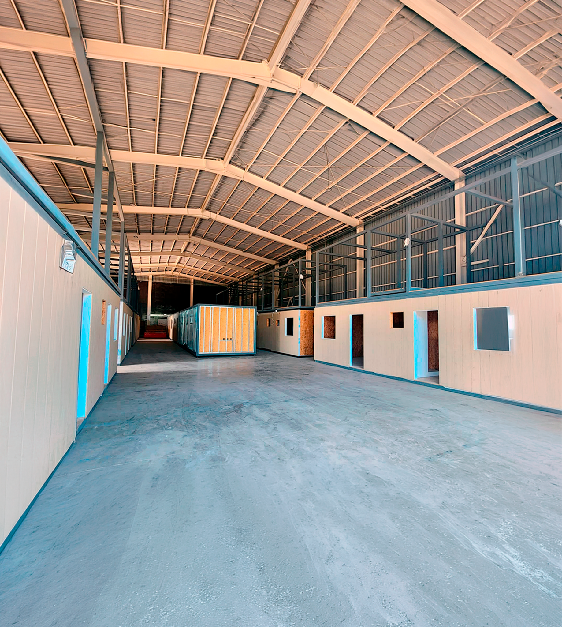 Vista interior panorámica de planta de fabricación de infraestructura modular técnica. Galpón industrial de alta capacidad para construcción simultánea de salas eléctricas y módulos BESS en REMAC.